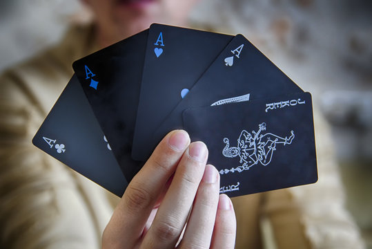 Poker card game combination of black colored playing cards named Poker: 4 aces and joker in hand of man (croupier or magician)