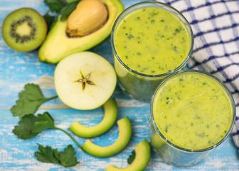 Two glass cups with a smoothie of avocado, banana, kiwi and herbs on a blue vintage table. Diet vegetarian food.