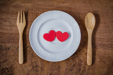 Couple red heart shape on white plate with wooden spoon and fork on wooden table. Concept for valentines day love celebration