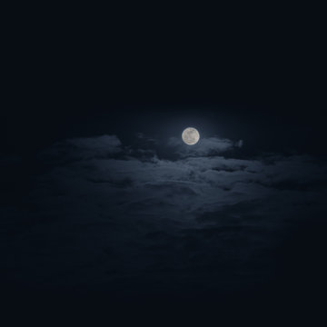 Dramatic photo of a nighttime sky with clouds and the moon and dark blue background.
