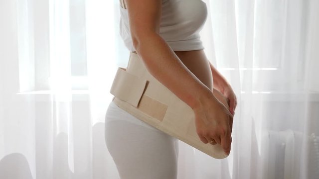 future mother tightening bandage for pregnant women and touching big tummy in slow motion on white background