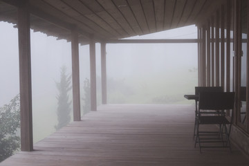Fototapeta premium wood balcony in mist & fog. terrace in cold autumn evening. chair in mysterious forest.