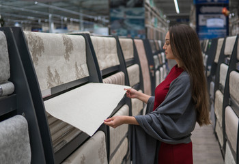 smart customer woman buying wallpaper in the supermarket design and repair department. she unwinds the rolls and chooses the best.
