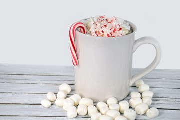 hot chocolate drink in white mug with marshmallows and whipped cream with Christmas candy cane on...