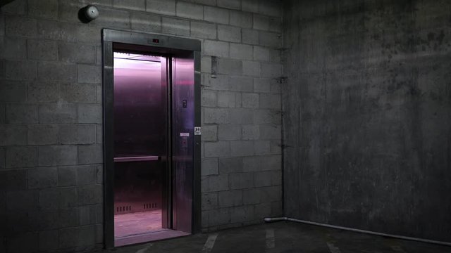 An Elevator door opens in the basement ground level of dark parking garage