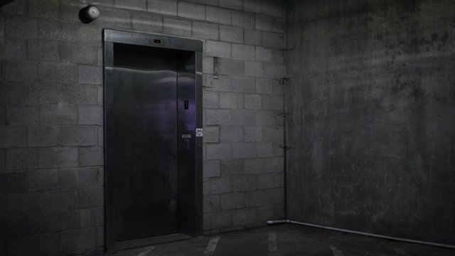 An Elevator door closes in the basement ground level of dark parking garage