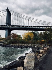 Manhattan bridge and rocks on riverside with cloudy sky
