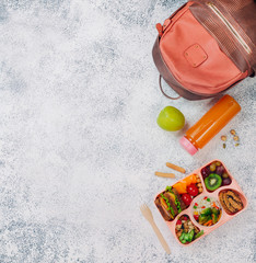 Open lunch box with healthy food on the grey background near backpack