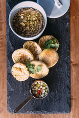 Grilled pork topped with cilantro and served with an English muffin, pickled vegetables and crumbed pistachios. served in black stone plate.