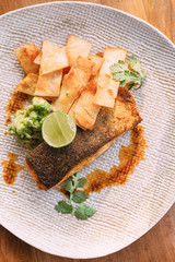 Grilled well done salmon steak served with pistachio sauce and sliced lime topping with fried sticks.