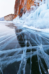 Winter landscape of the frozen Lake Baikal. The cliffs of the Olkhon Island with red lichen are covered with crust of ice