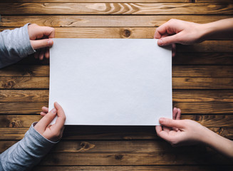 Hands hold a white sheet of paper. Clean sheet of paper on a wooden background.