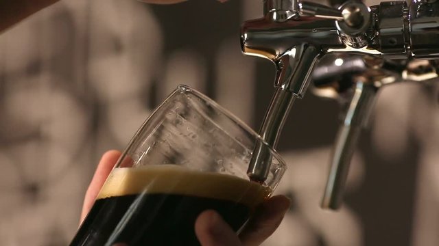 The bartender pours a dark beer in glass close-up.