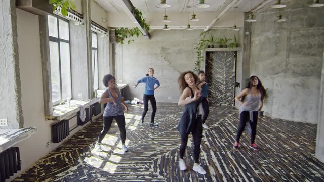 Crane shot of happy female dance teacher with curly hair dancing zumba with female students in studio, then high-fiving them