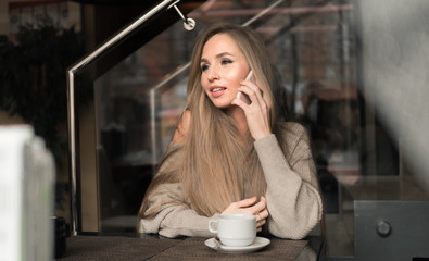 Young woman at cafe drinking coffee and talking on the mobile phone