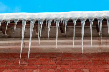White snow on the roof of a red brick house and icicles hanging from a slate roof