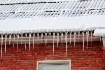 White snow on the roof of a red brick house and icicles hanging from a slate roof