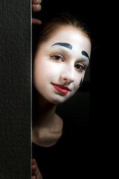 The girl wth makeup of mime hiding behind the wall