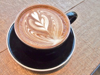 Cup of coffee on the wooden table with latte art, top view.