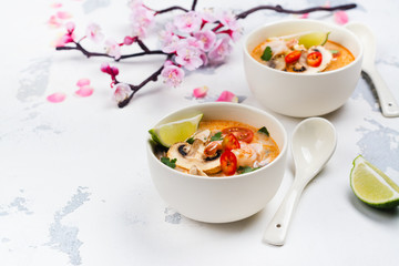 Traditional Tom Yum soup with blooming sakura branch on white stone table