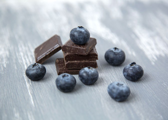 Close up Dark Chocolate Stack and Fresh Organic Blueberries on Wooden Background Natural Light Selective Focus