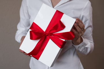 A woman in a white shirt is holding a gift, a white box with ipad inside and decorated with a red bow.