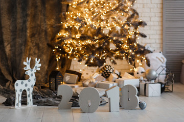 Sign symbol 2018 year under Christmas Tree decorated with golden garland and deer.