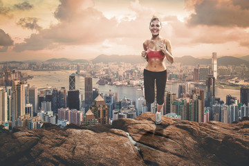 Fit blonde girl jogging up to the rocks hill over the metropolis - obrazy, fototapety, plakaty