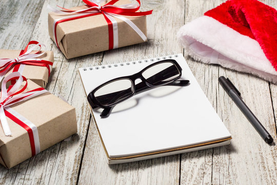 Christmas and Business Items with Copy Space Santa Cap Notepad Pen Glasses and decorated Gift Boxes