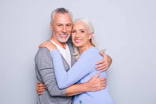 Portrait of delightful tender gentle elderly spouses who are relaxing, hugging, they have perfect ideal beaming shiny smiles, isolated on grey background