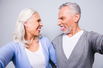 Close up photo of crazy happy mad old people, they are taking a selfie on a tablet, isolated on grey background