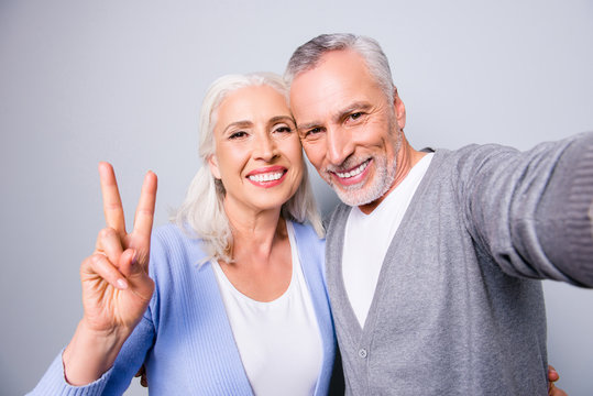 Happy sweet memories! Close up photo of senior couple showing two fingers and taking a selfie, isolated on grey background