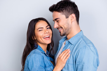 Close up portrait of caucasion lovely couple - smiling man with bristle looking at his funny, cute woman who laugh, blink and looking at camera  standing over grey background - obrazy, fototapety, plakaty
