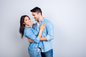 Portrait of sweet hispanic cute lovers, bearded man hugging woman and looking at her, pretty woman looking at camera over grey background