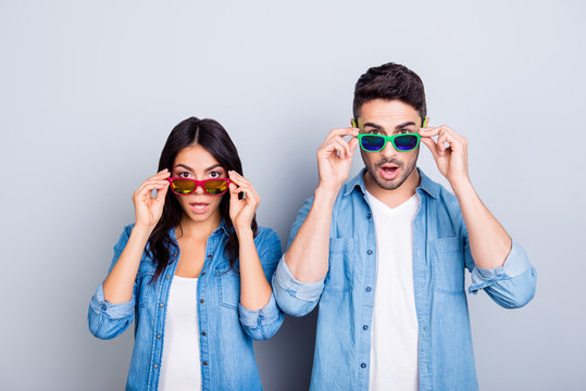 Oh my God! Shocked partners  with wide opened mouths and eyes peering out summer glasses  over grey background