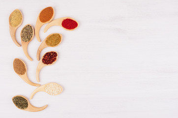 Assortment colorful powdered spices in bamboo spoons as decorative quaint branch. White wood background, top view, copy space.