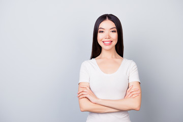 Fototapeta premium Portrait of cute confident pretty woman with beaming smile with folded hands, standing over grey background with copy space