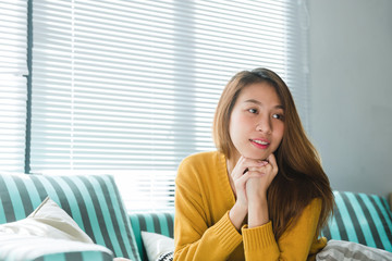 Portrait of happy home owner asian woman with perfect teeth smiling sitting on sofa in the living room in house interior. Relaxing asian woman sitting comfortable in sofa lounge chair smiling happy.