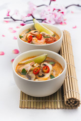 Traditional Tom Yum soup with blooming sakura branch on white stone table