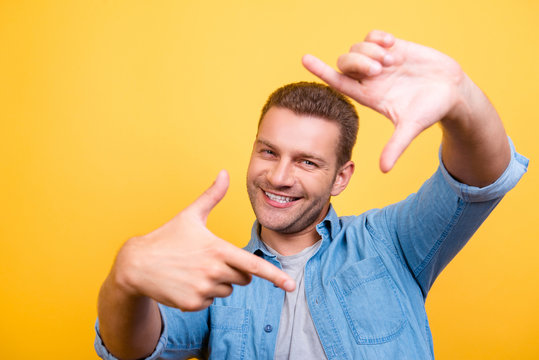 Closeup of young, happy man with stubble making diagonal frame in front of face with fingers, over yellow background