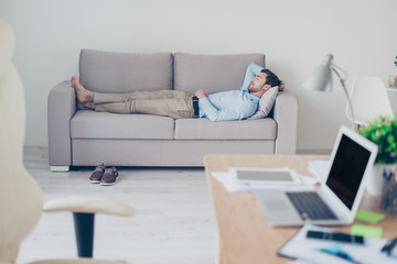 Concept of necessity of  having a rest while working. Tired exhausted manager clothed in formal-wear is sleeping on a sofa in his modern office - obrazy, fototapety, plakaty