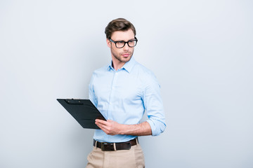 Close up portrait with copy space of attractive, clever, perfect man in shirt, pants, glasses holding clip board looking to the side over grey background