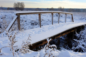 Beautiful winter landscape. Small wooden pedestrian bridge under the snow.