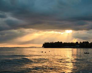 Sun breaking through low hanging storm clouds during sunset over Lake Constance
