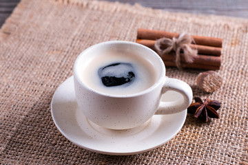 Coffee cup, cinnamon sticks on wooden table on brown background