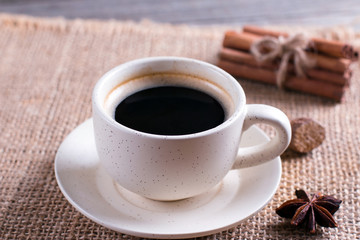 Cup of black coffee in cup, star anise, cinnamon sticks on wooden table