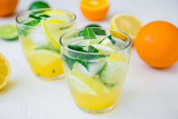 Citrus lemonade with lime, mint leaves and lemon in glasses on white table