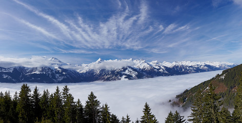 Panoramic view to foggy valley and Alps Mountains with blue sky and white fleecy clouds in background at Zell Am See Austrian Schmitten ski resort in march month