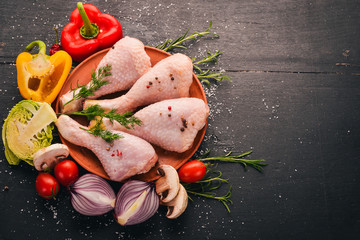 Raw chicken legs with fresh vegetables and rosemary and spices on a black wooden background. Top view. Free space for text.