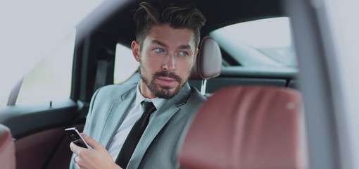 Happy young businessman using mobile phone in back seat of car